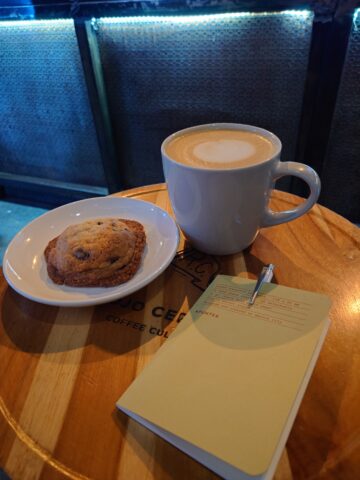 Taza de café en latte, galleta de avena con chispas de chocolate y libreta de notas
